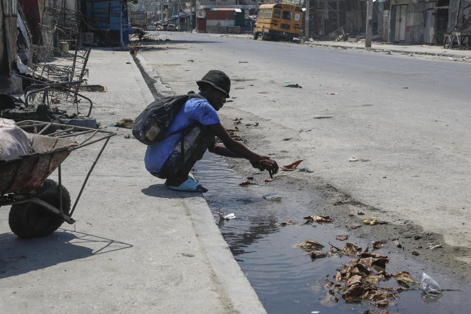 A man washes his hands in a puddle of runoff water after searching for salvageable things from burned-out cars at a mechanic shop set on fire during gang violence in Port-au-Prince, Haiti, Monday, March 25, 2024. (AP Photo/ Odelyn Joseph)