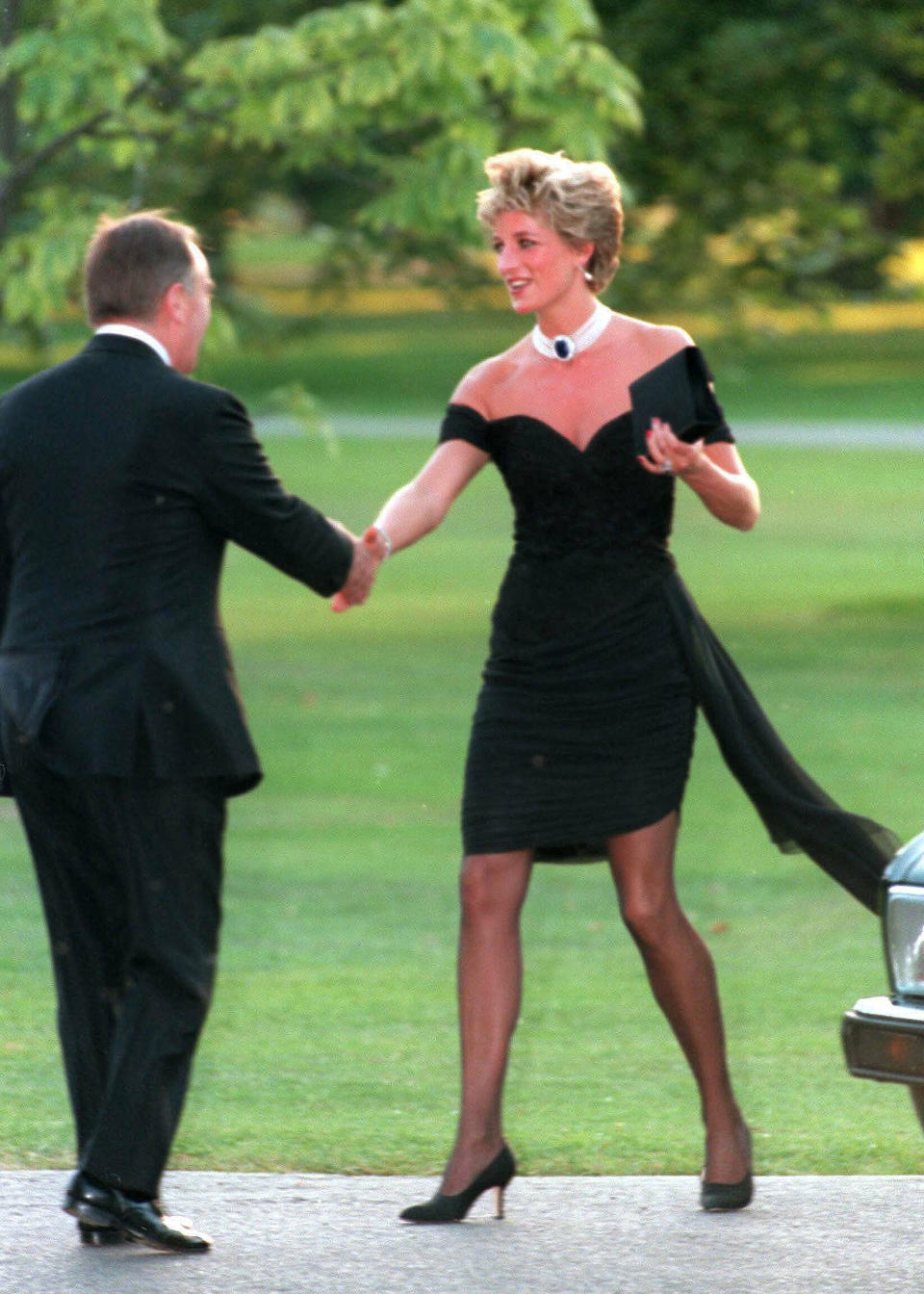 Princess Diana wearing a stunning off-the-shoulder short black dress and high heels.