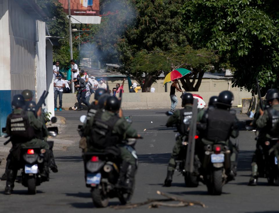 Anti-government protesters take cover from tear gas fired by Bolivarian National guards riding motorbikes during clashes in Caracas, Venezuela, Saturday, March 22, 2014. Two more people were reported dead in Venezuela as a result of anti-government protests even as supporters and opponents of President Nicolas Maduro took to the streets on Saturday in new shows of force. (AP Photo/Fernando Llano)