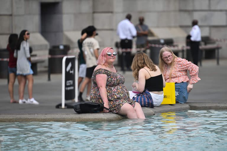 Pessoas se refrescam com os pés na água na fonte de Trafalgar Square, no centro de Londres, em 13 de julho de 2022, durante uma onda de calor.  (Foto de JUSTIN TALLIS/AFP)