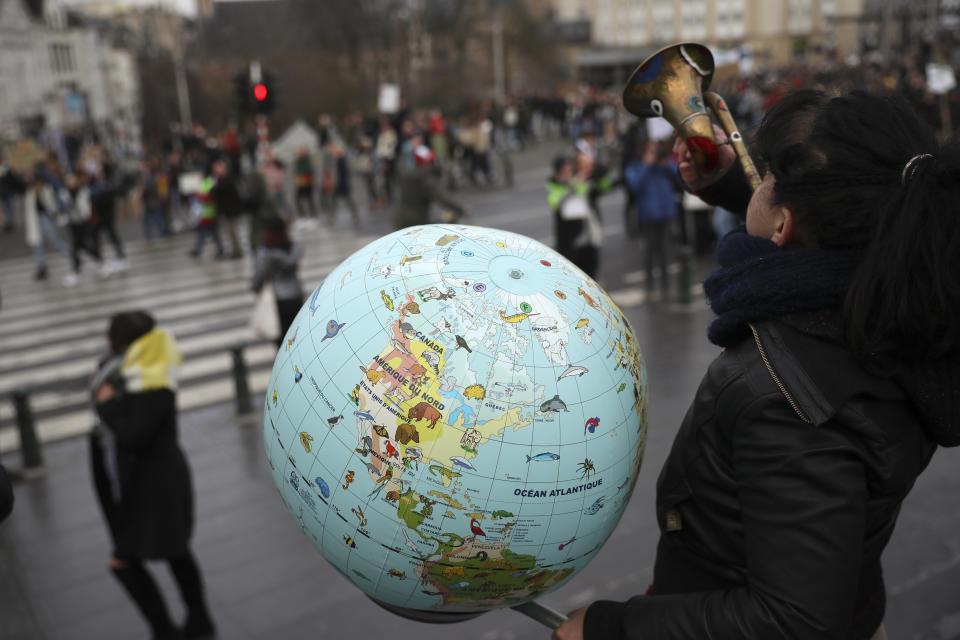 A woman holds a globe as she plays a trumpet during a climate change protest in Brussels, Thursday, Jan. 31, 2019. Thousands of teenagers in Belgium have skipped school for the fourth week in a row in an attempt to push authorities into providing better protection for the world's climate. (AP Photo/Francisco Seco)