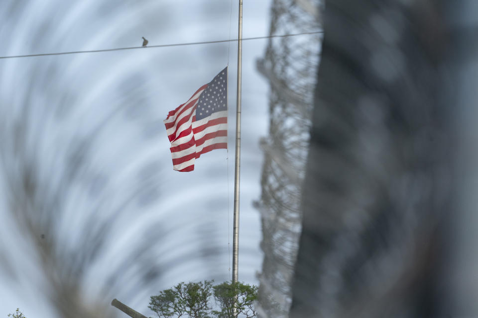 In this photo reviewed by U.S. military officials, a flag flies at half-staff in honor of the U.S. service members and other victims killed in the terrorist attack in Kabul, Afghanistan, as seen through a fence at Camp Justice, Sunday, Aug. 29, 2021, in Guantanamo Bay Naval Base, Cuba. Camp Justice is where the military commission proceedings are held for detainees charged with war crimes. (AP Photo/Alex Brandon)