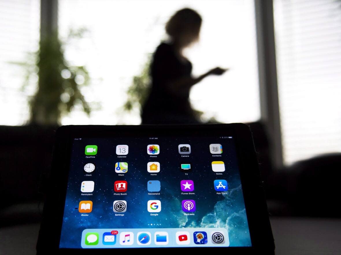 A person uses their smartphone as apps are shown on an iPad in Ontario in 2017. According to tech and legal experts, passing laws to address disinformation on social media is not that simple, and in some cases can lead to other problems. (Nathan Denette/Canadian Press - image credit)