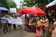 Anti-coup protesters hold signs that read "We Support NUG" that stands for ‘national unity government’ as they march on a street where vendors sell fresh products Saturday, April 17, 2021 in Yangon, Myanmar. Opponents of Myanmar’s ruling junta have declared they have formed an interim national unity government with members of Aung San Suu Kyi’s ousted cabinet and major ethnic minority groups.. (AP Photo)