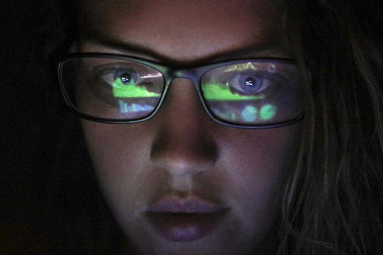 A woman's face with financial graphs from a computer reflected in her glasses.