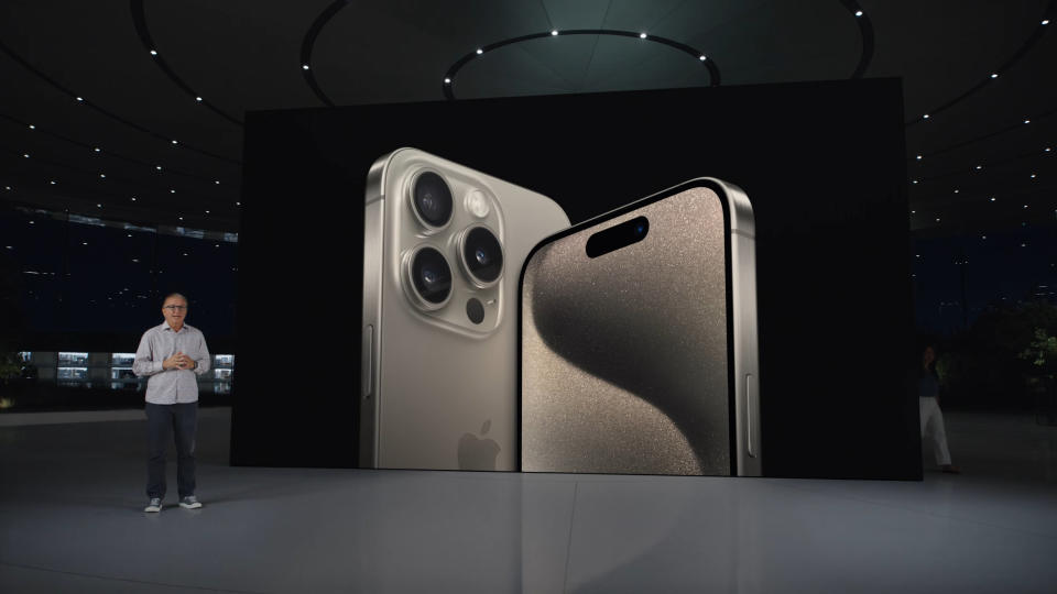 The natural titanium Apple iPhone 15 on a screen in a futuristic looking warehouse