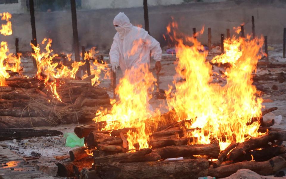 A social worker wearing PPE walks amid burning funeral pyres as he performs last rites of the Covid-19 victims in Bhopal - SANJEEV GUPTA/EPA-EFE/Shutterstock