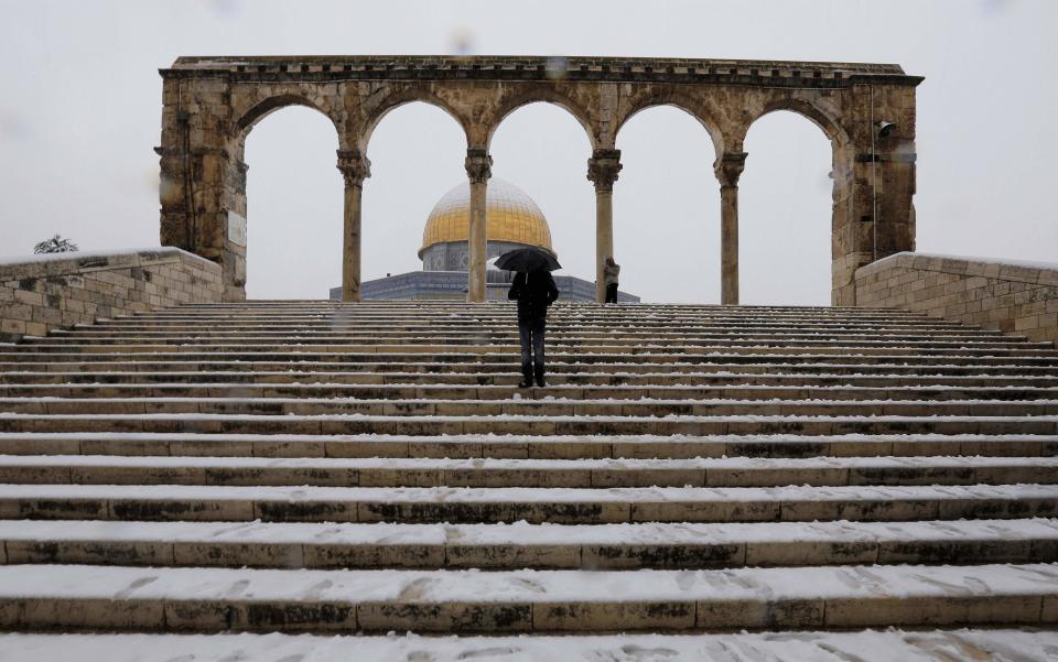 A man holding an umbrella stands in front of the Dome of the Rock in the compound known to Muslims as Noble Sanctuary and to Jews as Temple Mount, in Jerusalem's Old City during a snowstorm in winter December 12, 2013. REUTERS/Ammar Awad (JERUSALEM - Tags: RELIGION ENVIRONMENT)