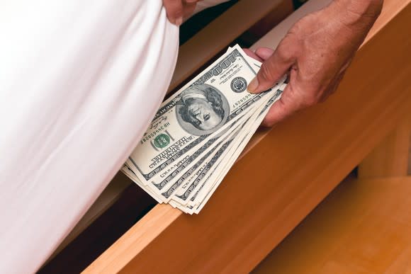 A person placing hundred dollar bills under their bed.