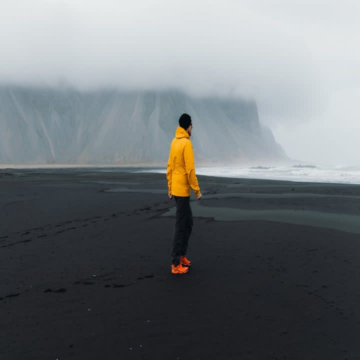 A man walks across a beach towards the water underneath an overcast sky