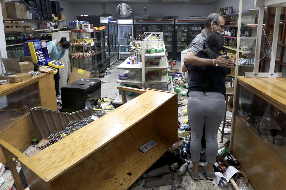 Yogi Dalal hugs his daughter, Jigisha, after she arrived Monday, Aug. 10, 2020 at the family food and liquor store, as his other daughter, Kajal, left, bows her head, after the family business was vandalized in downtown Chicago. (AP Photo/Charles Rex Arbogast, File)