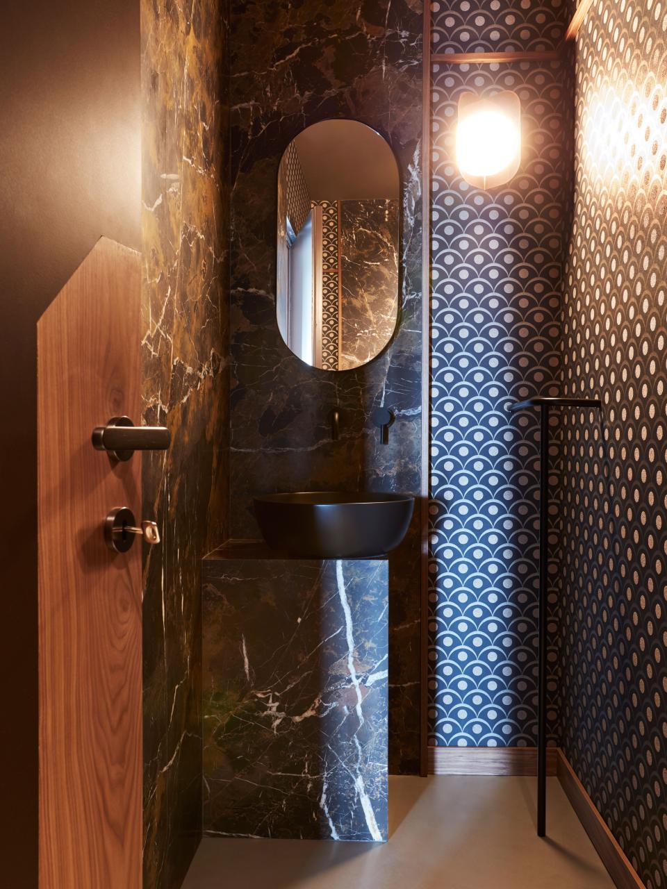 The guest bathroom plays with asymmetry and contrasts between materials such as the brown marble and the wallpaper with a groovy geometric pattern.