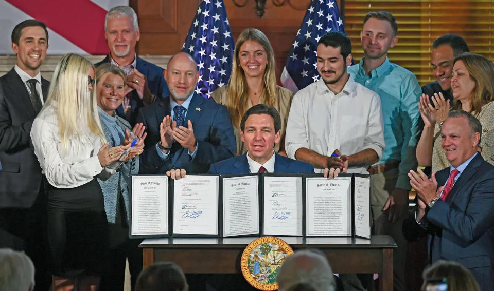 Gov. Ron DeSantis holds up three bills that he signed May 15, 2023. One of them bans the use of state funds for DEI programs at Florida's universities and college. New College President Richard Corcoran is at right.