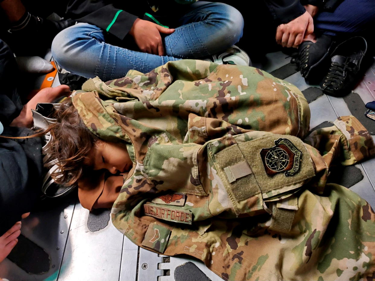 An Afghan child sleeps on the cargo floor of a U.S. Air Force C-17 Globemaster III, kept warm by the uniform of Airman First Class Nicolas Baron, C-17 loadmaster, during an evacuation flight from Kabul, Afghanistan, August 18, 2021.  (U.S. Air Force/1st Lt. Mark Lawson/Handout via Reuters)