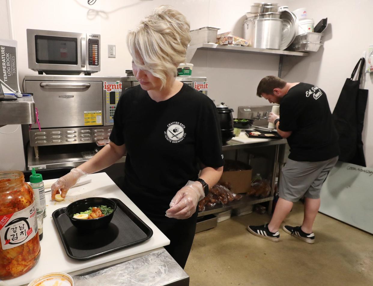 Andi Lisy of Crafted Eats at Ignite Brewing Co. puts together Ignite the Ramen, a fusion ramen bowl, in the kitchen at Ignite in Barberton on Friday as her brother John Hawkins works in the background.