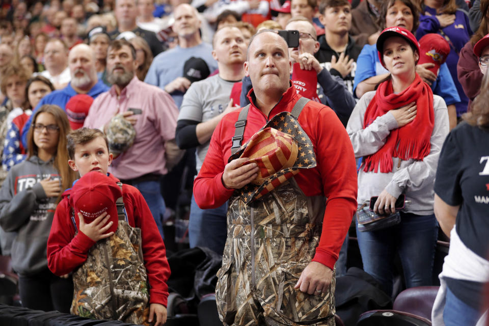 A man and boy dressed in chest waders hold their hats to their hearts during the Pledge of Allegiance at the start of a campaign rally for President Donald Trump in Bossier City, La., Thursday, Nov. 14, 2019. (AP Photo/Gerald Herbert)