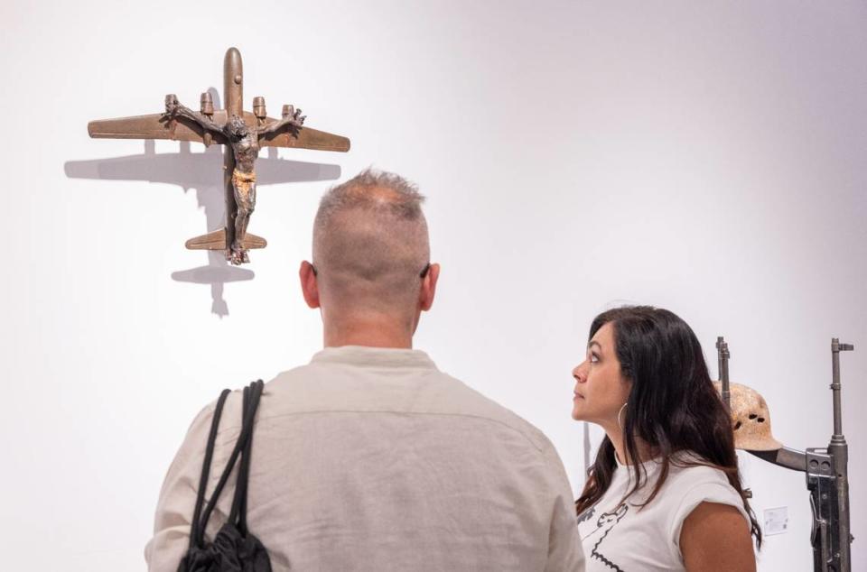 Guests view a sculpture by artist Al Farrow that depicts a Christ-like figure crucified to a fighter jet. Farrow criticizes how religion is used to justify war in his artwork.