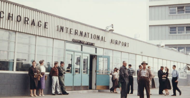 Group of people standing outside the Anchorage International Airport in a historical photo