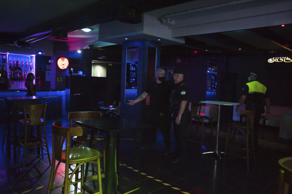 A police officer talks with an employee inside a nightclub In Fuengirola, near Malaga, Spain, Saturday, Aug. 8, 2020. The increase in Spain of coronavirus outbreaks associated with nightlife has set off alarms in recent days, mainly in tourist areas where pubs and discos are full before the summer tourist campaign. (AP Photo/Jesus Merida)