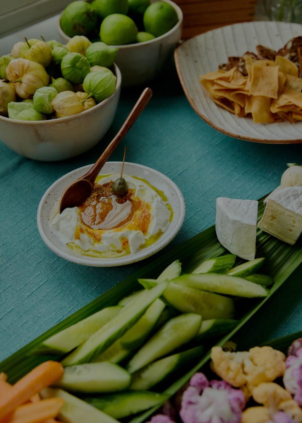 The abundant spread of sliced cucumbers, chunks of brie cheese, cauliflower florets, carrot sticks, and pita chips