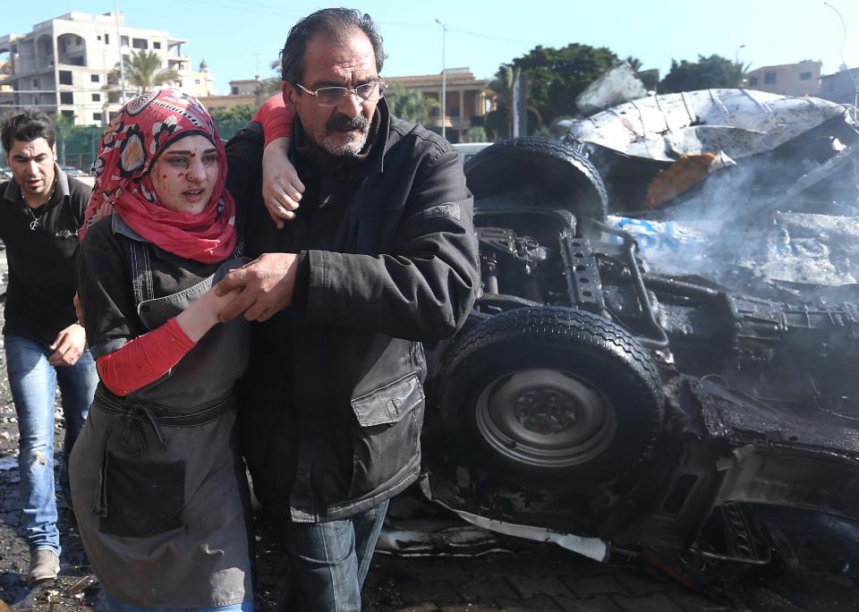 A Lebanese man helps an injured woman, as they pass the site of an explosion, near the Kuwaiti Embassy and Iran's cultural center, in the suburb of Beir Hassan, Beirut, Lebanon, Wednesday, Feb. 19, 2014. The bombing in a Shiite district in southern Beirut killed several people on Wednesday, security officials said — the latest apparent attack linked to the civil war in neighboring Syria that has killed and wounded scores of people over the last few months. (AP Photo/Hussein Malla)