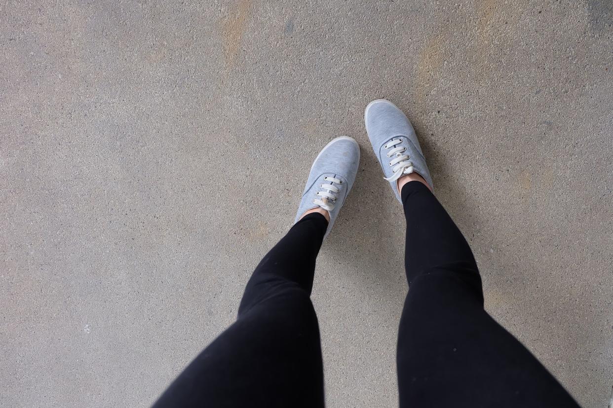 Beautiful Gray Shoes Footwear of Accessories. Young Fashion Woman's Legs in Black Jeans and Gray Sneakers on Street Road Background.