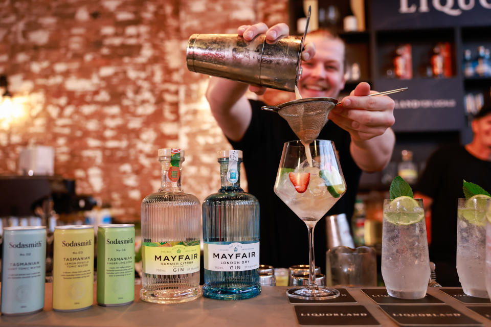 A man pouring a cocktail beside bottles of gin and cans of tonic