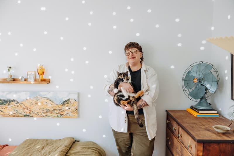 Dweller holds cat in white bedroom with light scattered on wall.