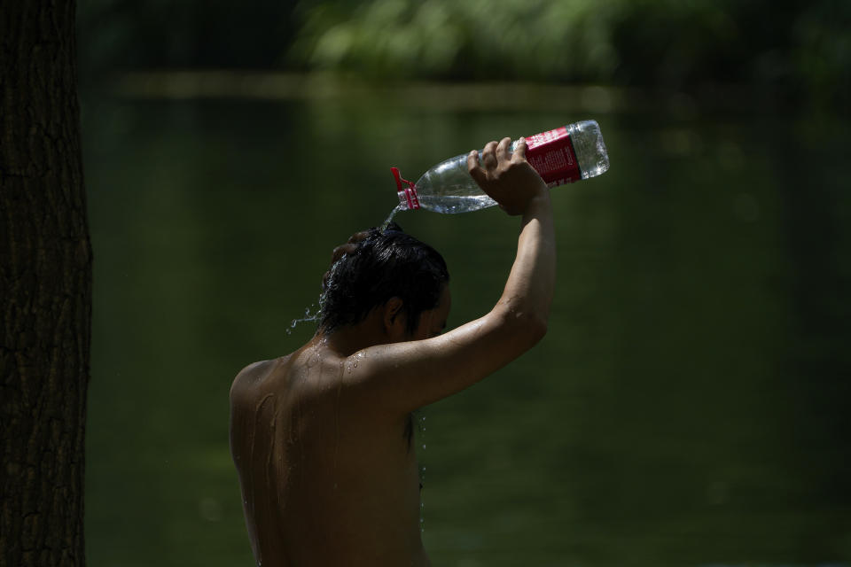 A resident tosses water to himself as residents cool off on a sweltering day at an urban waterway in Beijing, Monday, July 10, 2023. Rescuers were looking Monday for several people missing in a landslide triggered by torrential rains while employers across much of China were ordered to limit outdoor work due to scorching temperatures as the country struggled with heat, flooding and drought. (AP Photo/Andy Wong)