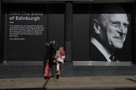 Isabella Disley greets her mother Tara Lynn and her dog Coco next to a portrait of Prince Philip, which adorns a window of a department store in Windsor, England, Friday, April 16, 2021. Prince Philip husband of Britain's Queen Elizabeth II died April 9, aged 99, his funeral will take place Saturday at Windsor Castle in St George's Chapel. (AP Photo/Alastair Grant)