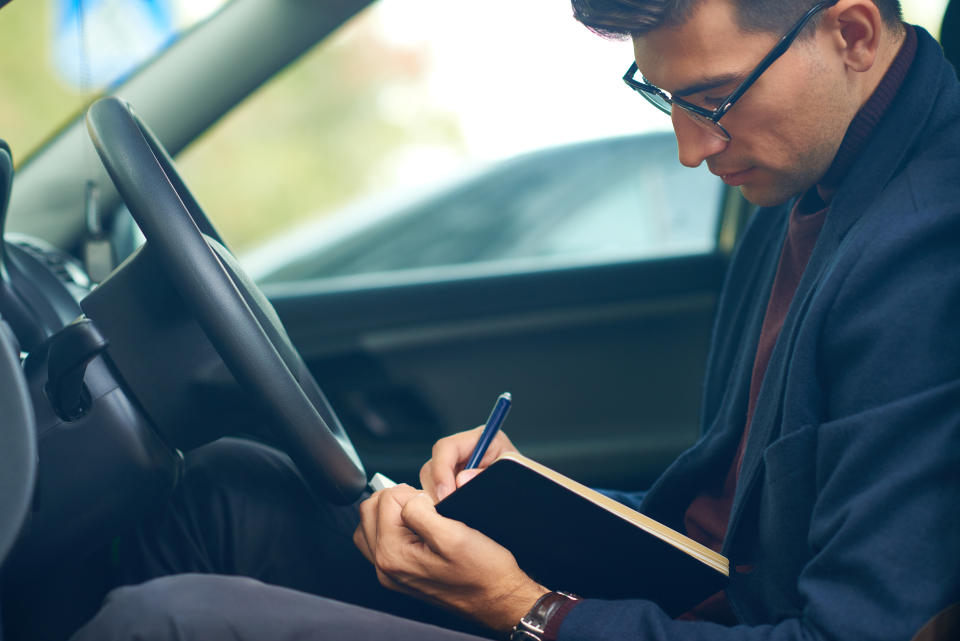 Man in the driving seat makes notes in a logbook for tax purposes.