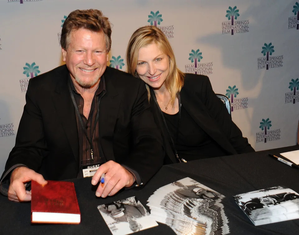 A man and woman smile while seated behind a table at Palm Springs International Film Festival, with autographed photos in front of them. Names unknown