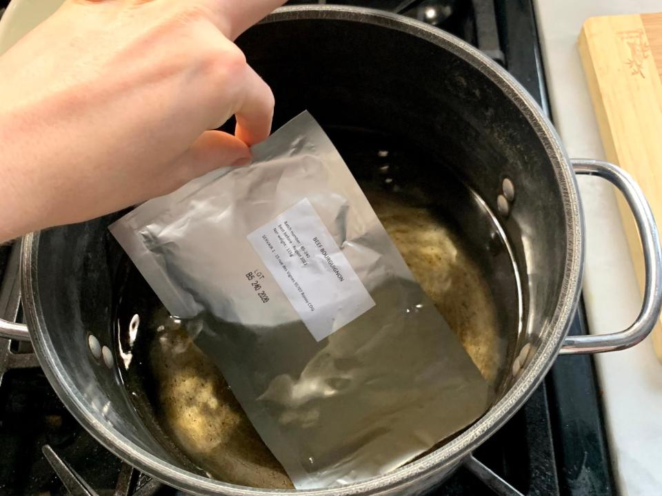 hand dropping astronaut food foil pouch into pot of hot water on stove