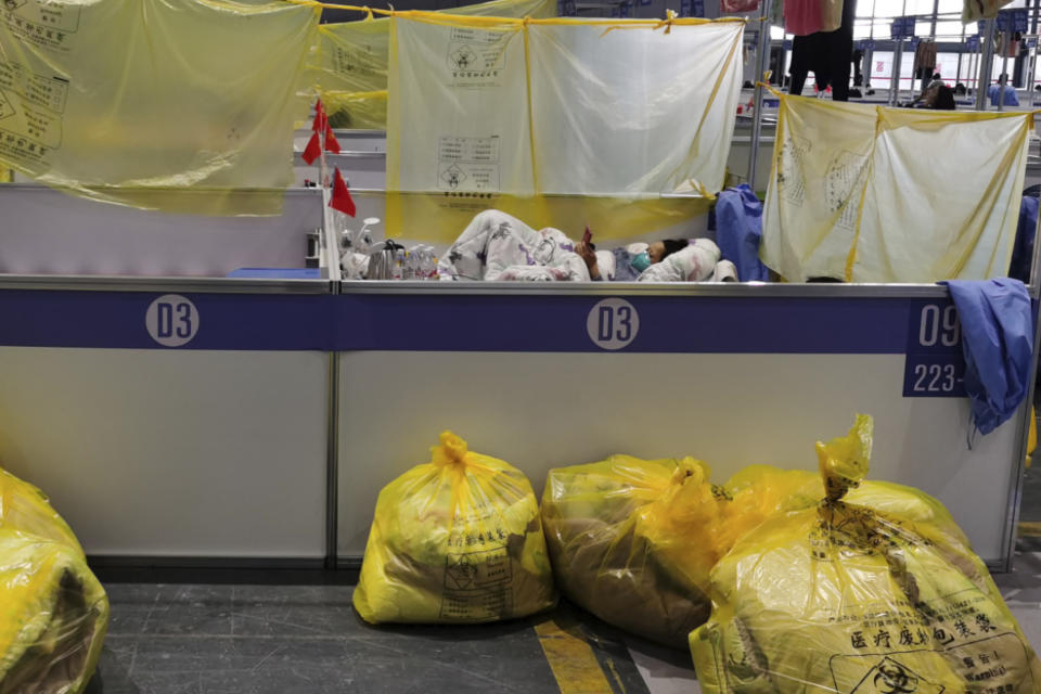 A resident rests near bags of marked as medical waste at a temporary hospital converted from the National Exhibition and Convention Center to quarantine COVID-positive people in Shanghai, China on April 18, 2022. Interviews with family members of people testing positive for COVID-19, a phone call with a government health official and an independent tally raise questions about how Shanghai calculates virus cases and deaths, almost certainly resulting in a marked undercount. (Chinatopix via AP)