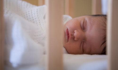 A baby lies sleeping in her cot