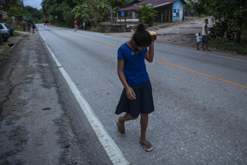 A girl carries a plate with corn for tortillas near an army checkpoint in San Luis Peten, Guatemala, Saturday, Oct. 3, 2020. Early Saturday, hundreds of migrants who had entered Guatemala this week without registering were being bused back to their country's border by authorities after running into a large roadblock. (AP Photo/Moises Castillo)