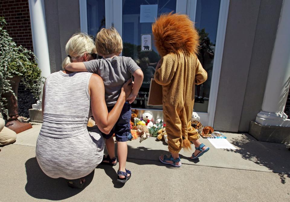 Sarah Madison (L) holds her son Beckett, 3, as her daughter Quinn, 5 (in costume), look at stuffed animals at the doorway of River Bluff Dental clinic in protest against the killing of "Cecil" a famous lion in Zimbabwe, in Bloomington, Minnesota July 29, 2015. (REUTERS/Eric Miller)