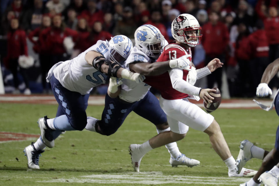 North Carolina State quarterback Devin Leary (13) is tackled by North Carolina defensive lineman Raymond Vohasek (51) and linebacker Tomon Fox (12) during the first half of an NCAA college football game Friday, Nov. 26, 2021, in Raleigh, N.C. (AP Photo/Chris Seward)