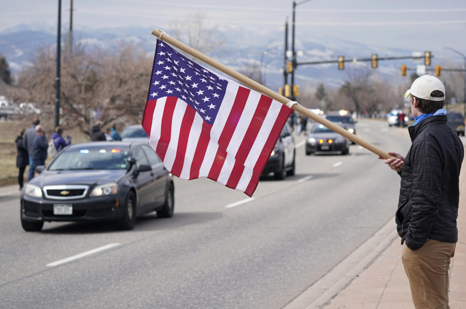 Thalin Di Paolo holds an American flag as a procession of emergency vehicles heads down Foothills Parkway to lead a hearse carrying the body of a Boulder, Colo., Police Department officer who was one of 10 victims in the mass shooting at a King Soopers grocery store Wednesday, March 24, 2021, in Boulder, Colo. Boulder Police Department Officer Eric Talley was killed responding to the shooting attack at the supermarket on Monday. (AP Photo/David Zalubowski)