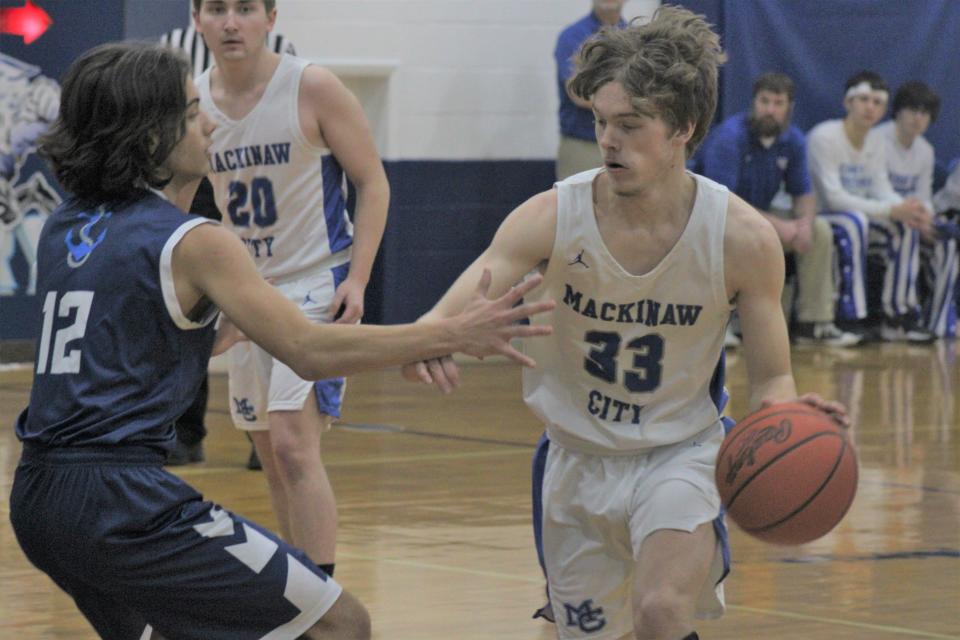 Mackinaw City senior Trystan Swanson (33) attempts to drive past Mackinac Island's Roman Gruits (12) during the first half of Monday's MHSAA Division 4 district boys basketball first-round game at Mackinaw City.