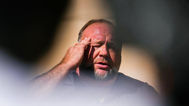 Alex jones silhouetted rubs his temple and glistens with sweat.