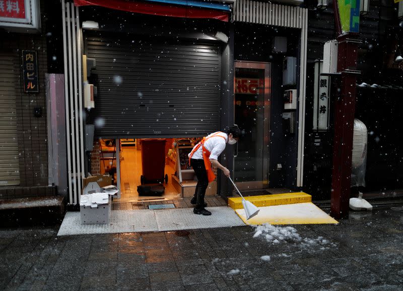 A shop employee wearing a protective face mask, following an outbreak of the coronavirus disease, tries to remove snow in a snow fall in Tokyo