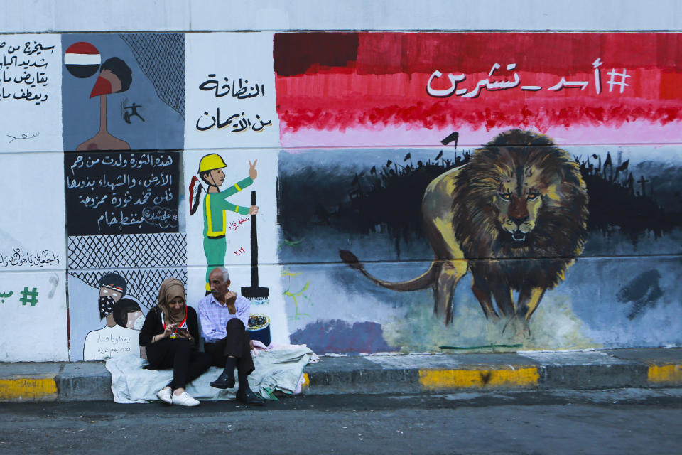 In this Sunday, Nov. 17, 2019 photo, people sit near graffiti in the Saadoun tunnel, in Baghdad, Iraq. The tunnel that passes under Baghdad’s landmark Tahrir Square has become an ad hoc museum for Iraq's revolution: Young artists draw images and murals that illustrate the country’s tortured past, and the Iraq they aspire to. Messages in Arabic, include, "Lion of October, Clean is from belief, They give us corruption, we give them a revolution and A revolution mixed with crude oil will not quell." (AP Photo/Hadi Mizban)
