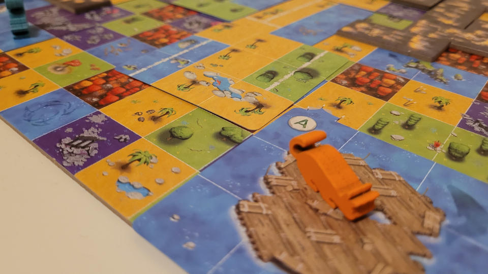 A cat token on a raft tile, with the board for Race to the Raft behind it