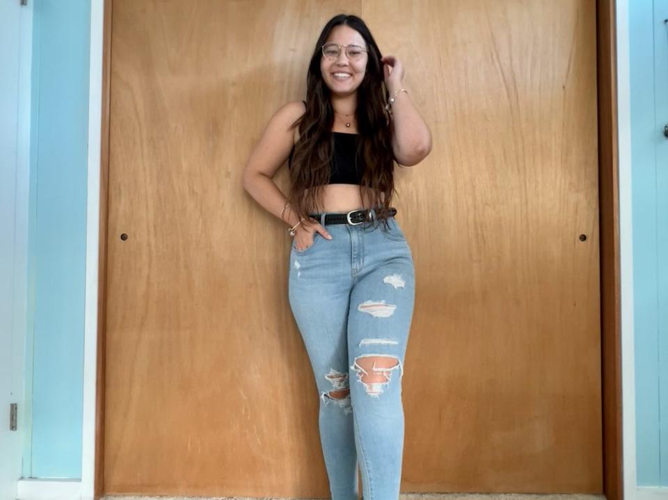 Ashley posing in front of wooden doors in black crop top and ripped jeans