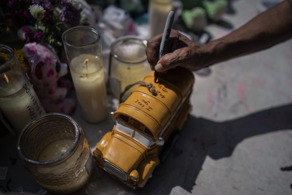 Josie Albrecht, a school bus driver who shuttled Uvalde's children to and from school writes a message on a toy school bus she brought to honor Rojelio Torres at a memorial site for those killed in a mass shooting at Robb Elementary School on Sunday, May 29, 2022, in Uvalde, Texas. "I love you and will miss you," she wrote on it, and drew a broken heart at the place where he used to sit, in the back. (AP Photo/Wong Maye-E)