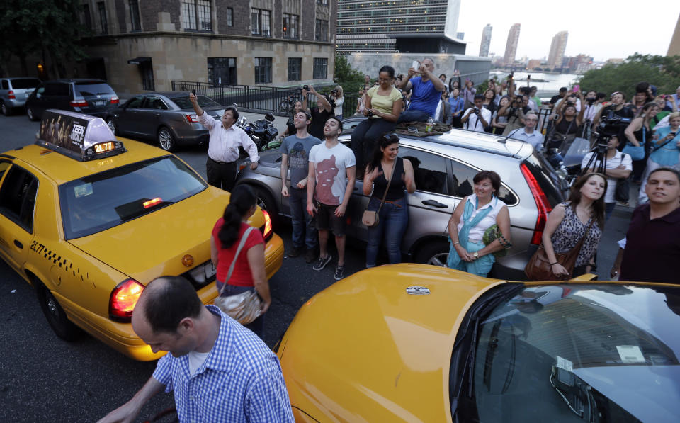 People gather in Tudor City waiting to watch the sun to set through the middle of the buildings on 42nd Street in New York's Manhattan borough during a phenomenon known as Manhattanhenge, Wednesday, July 11, 2012. Manhattanhenge, sometimes referred to as the Manhattan Solstice, happens when the setting sun aligns with the east-to-west streets of the main street grid. The term references Stonehenge, at which the sun aligns with the stones on the solstices in England. (AP Photo/Julio Cortez)