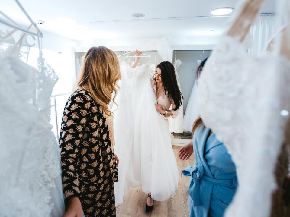 A bride holds up a dress to her friend in a bridal salon.