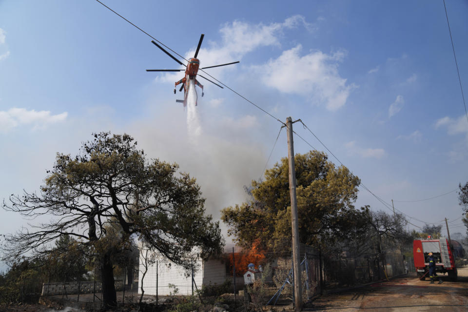 A helicopter drops water on a house during a wildfire in Thea area some 60 kilometers (37 miles) northwest of Athens, Greece, Thursday, Aug. 19, 2021. A major wildfire northwest of the Greek capital devoured large tracts of pine forest for a third day and threatened a large village as hundreds of firefighters, assisted by water-dropping planes and helicopters, battled the flames Wednesday. (AP Photo/Thanassis Stavrakis)