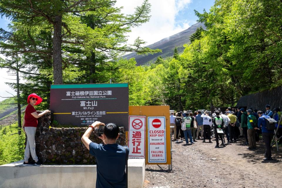 A tourist poses in front of the gate of a national park near the Fuji Subaru Line 5th station, which leads to the Yoshida trail for hikers climbing Mount Fuji (AFP via Getty)